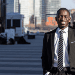 A student in New York wearing professional attire smiles with skyscrapers in the background.
