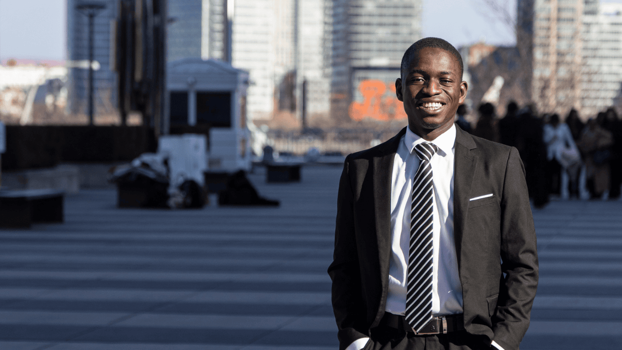 A student in New York wearing professional attire smiles with skyscrapers in the background.